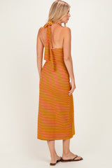 woman wearing a striped orange and yellow halter neck midi dress, showing the back view and styled with flat sandals