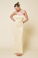 woman wearing a light yellow floral spaghetti strap maxi dress with a fitted silhouette and fringe detail at the bust