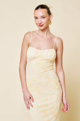 woman wearing a light yellow floral midi dress with thin straps and a fitted silhouette