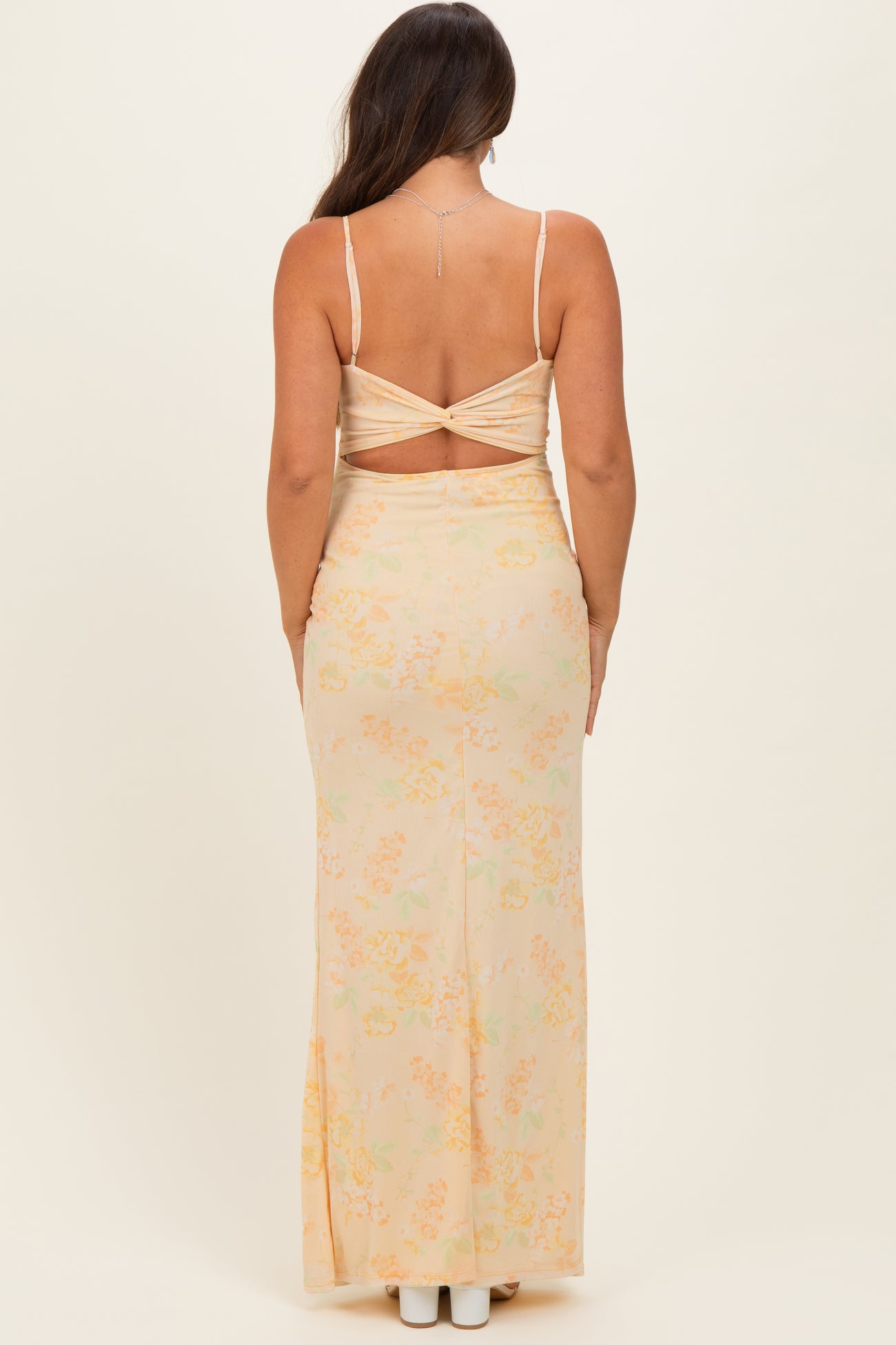 woman wearing a floral peach maternity maxi dress with a crisscross back and a visible baby bump