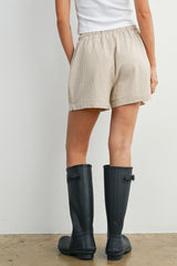 woman wearing beige striped shorts and black rubber rain boots, seen from the back