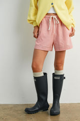 woman wearing red and white striped shorts, yellow cardigan, and black rubber rain boots with gray socks