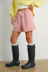 woman wearing red and white striped shorts with a drawstring and black rubber boots, styled with a yellow cardigan