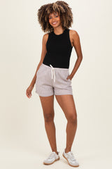 woman wearing a black sleeveless bodysuit and striped maternity shorts with pockets, standing and smiling