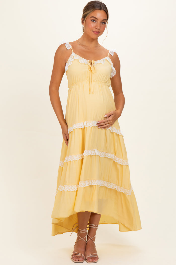 woman wearing a yellow tiered maternity dress with lace trim and a baby bump, standing gracefully