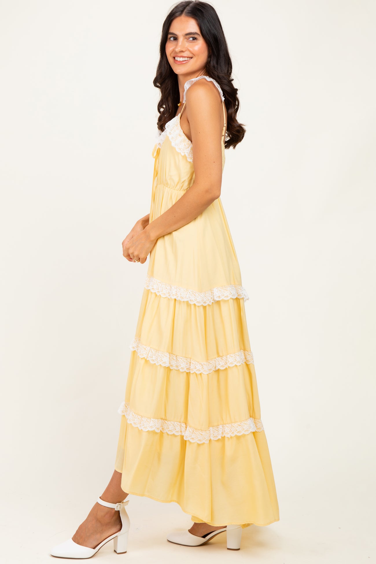 woman wearing a yellow tiered maxi dress with white lace trim and a bow detail, posing sideways with a smile