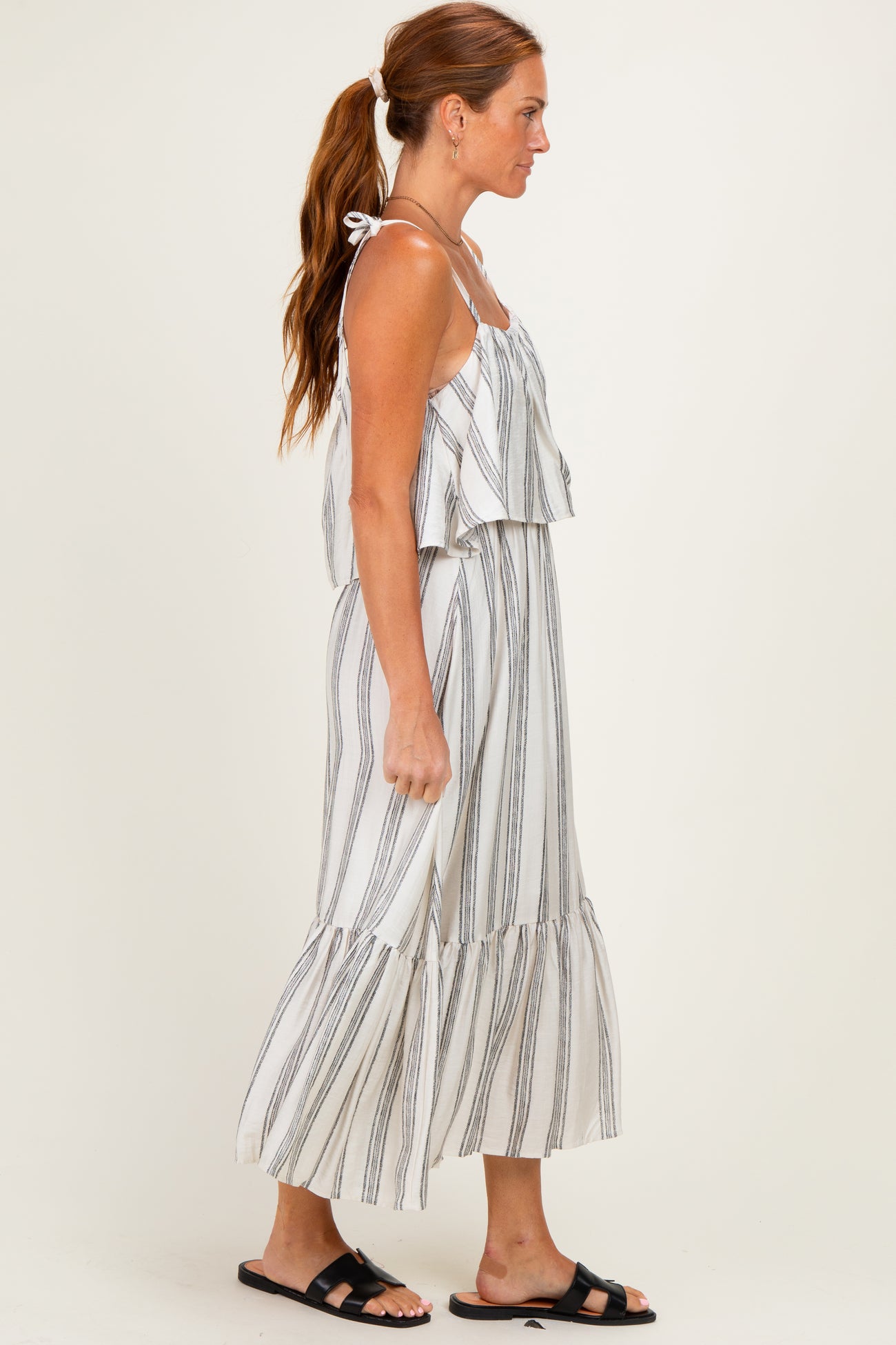 woman wearing a white and black striped maxi dress with ruffled layers and spaghetti straps, standing sideways