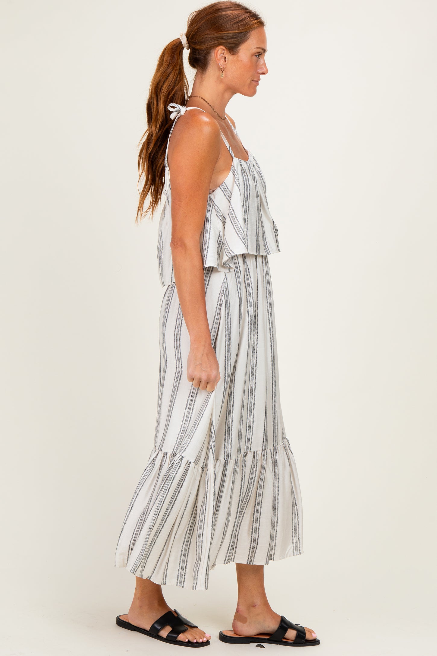 woman wearing a white and black striped maxi dress with ruffled layers and spaghetti straps, standing sideways