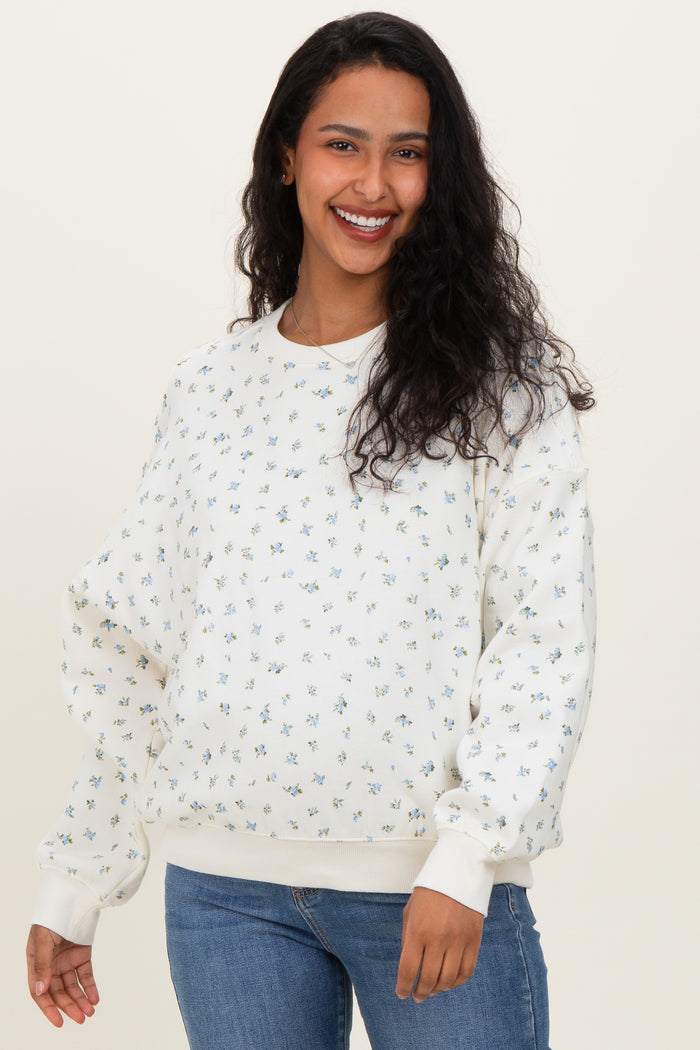 woman wearing a cream floral print maternity sweatshirt and blue jeans, displaying her baby bump