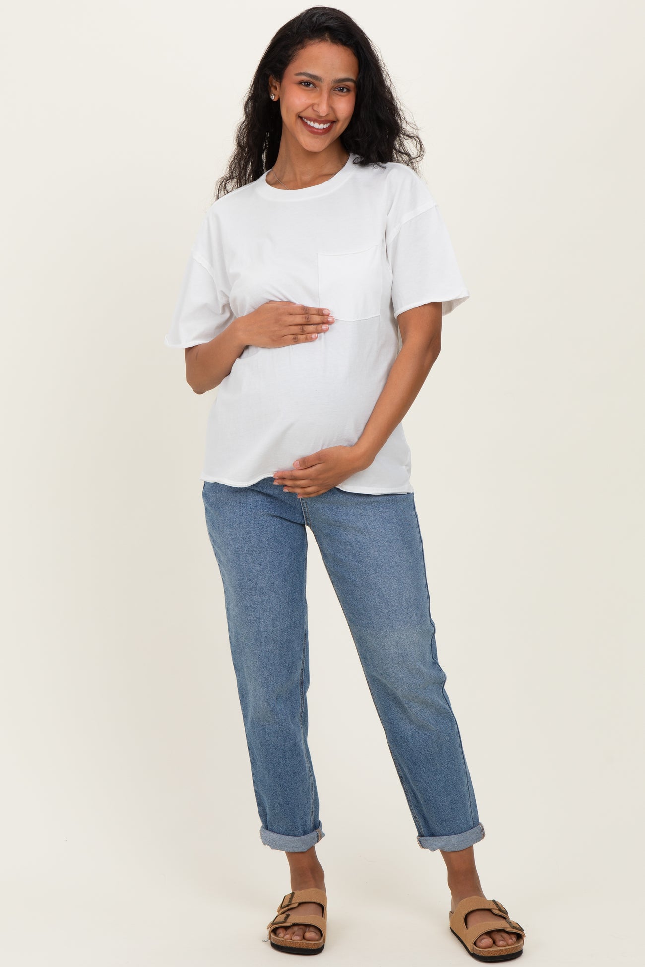 woman wearing a white maternity t-shirt and blue rolled-up jeans, gently holding her baby bump