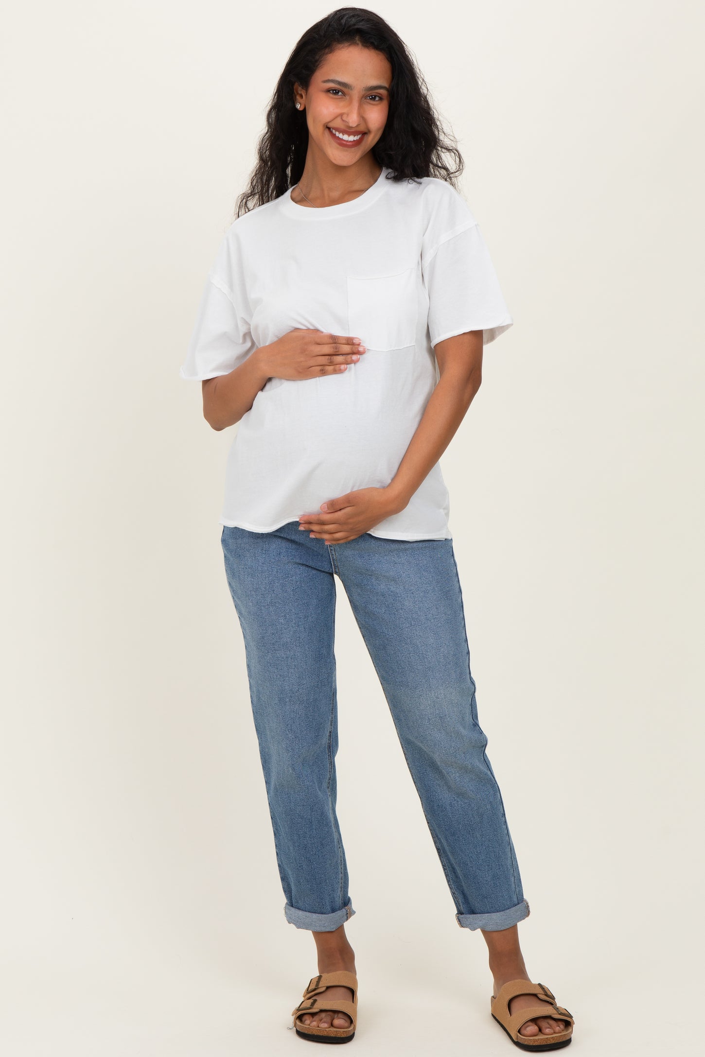 woman wearing a white maternity t-shirt and blue rolled-up jeans, gently holding her baby bump