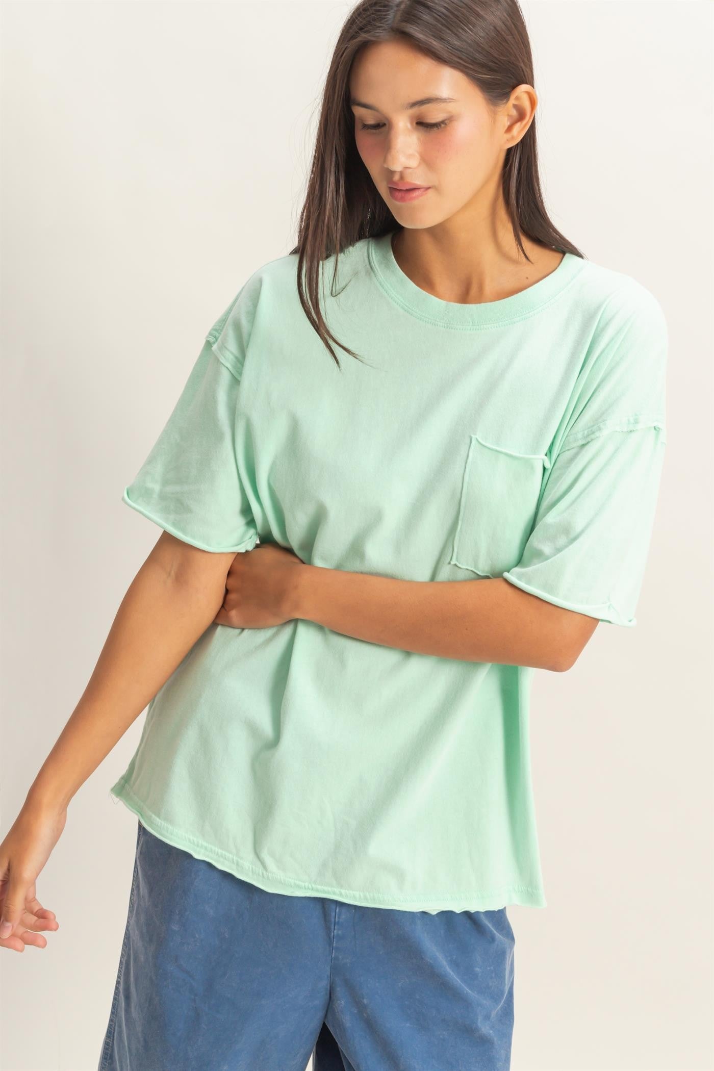 woman wearing a mint green oversized t-shirt with a pocket and short sleeves, paired with blue shorts