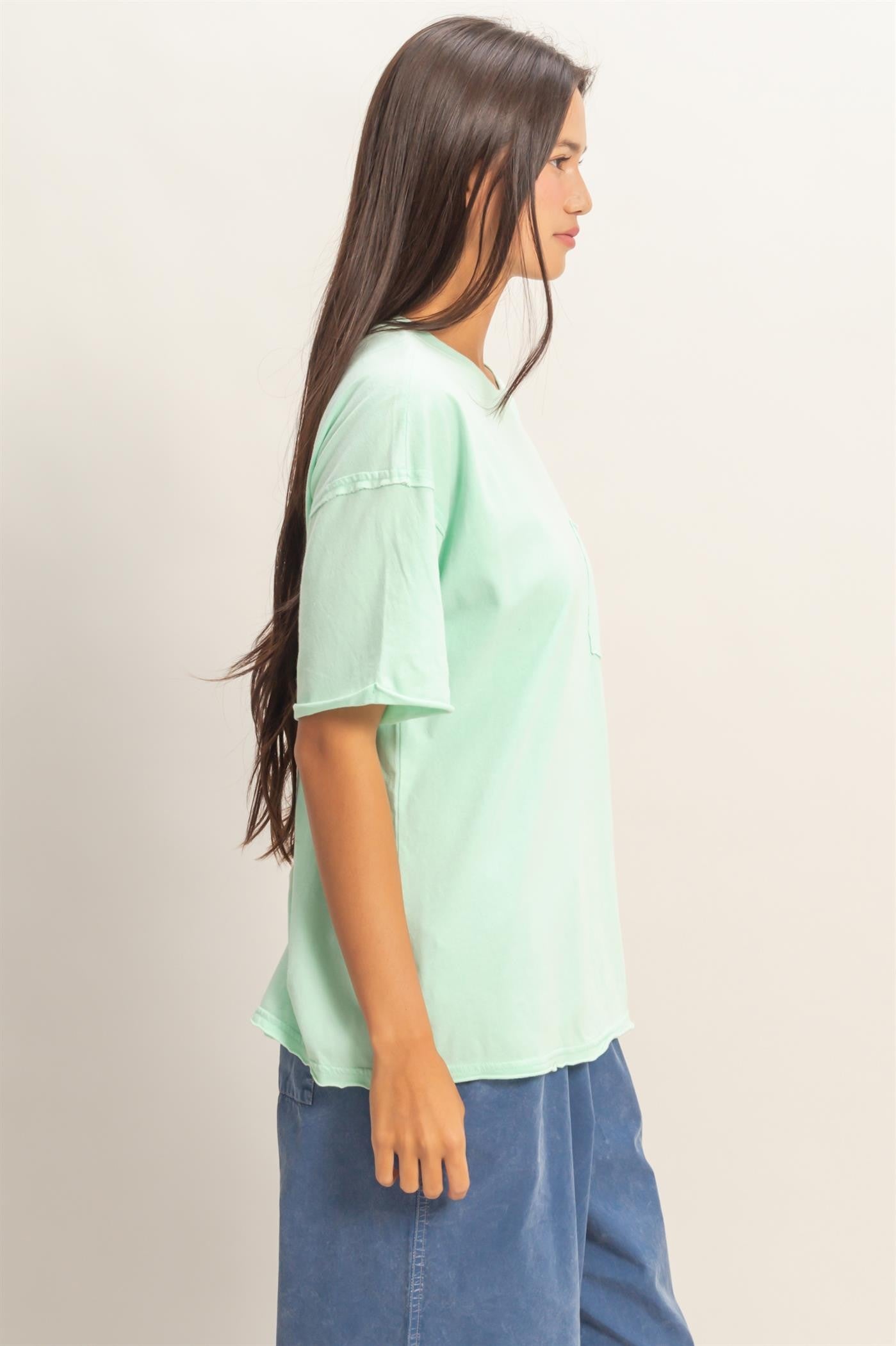 woman wearing a mint green short sleeve t-shirt with a relaxed fit and side pocket, paired with blue loose pants