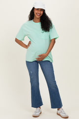 woman wearing a mint green oversized t-shirt and distressed flared jeans, showing her baby bump