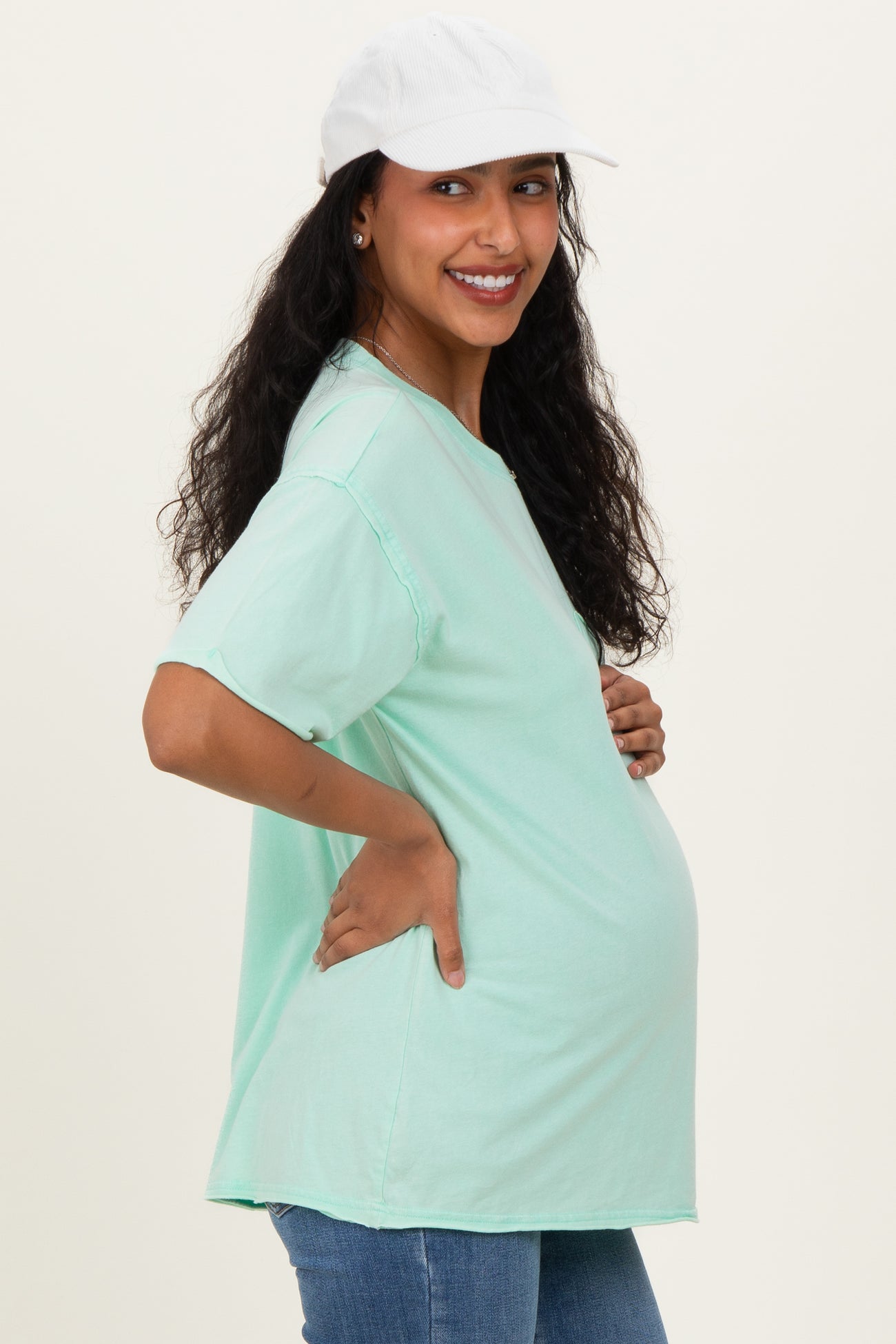 woman wearing a mint green oversized maternity t-shirt, posing with a visible baby bump and a white cap