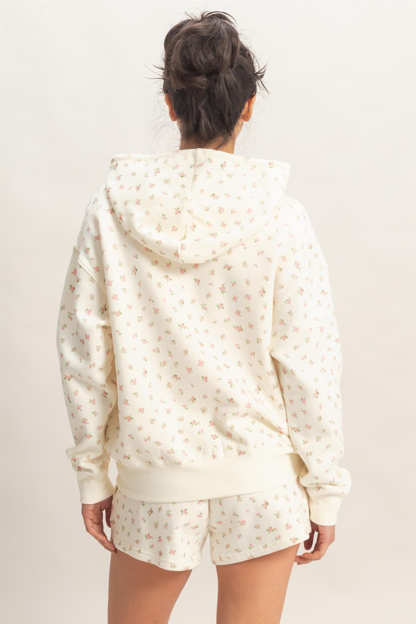 woman wearing a cream hoodie with a floral print and matching shorts, seen from the back