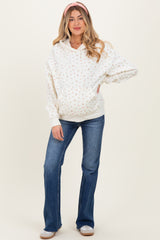 woman wearing a white floral maternity hoodie with a drawstring and blue flared jeans, showing her baby bump