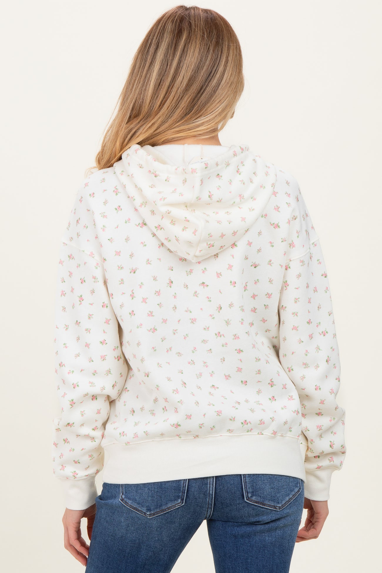 woman wearing a cream floral maternity hoodie with a hood, seen from the back, paired with blue jeans