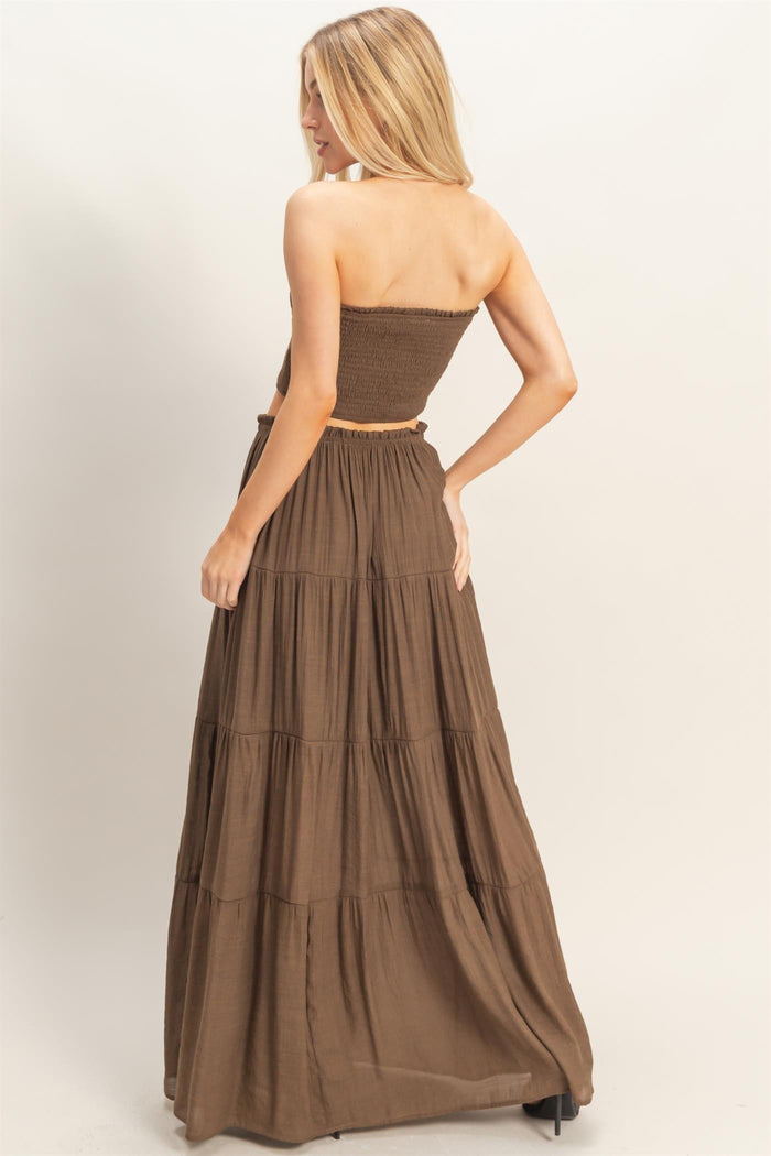 woman wearing a brown strapless crop top with a matching tiered maxi skirt, seen from the back