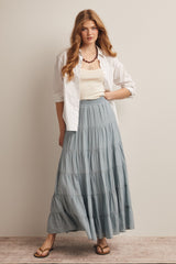 woman wearing a white button-up shirt and a light blue tiered maxi skirt with flat sandals and a statement necklace