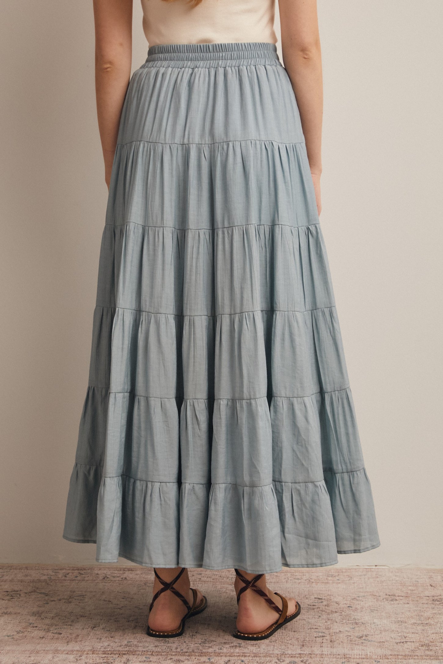 woman wearing a light blue tiered maxi skirt with an elastic waistband, seen from the back
