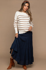 woman wearing a cream and brown striped maternity sweater and a navy maxi skirt, showing her baby bump