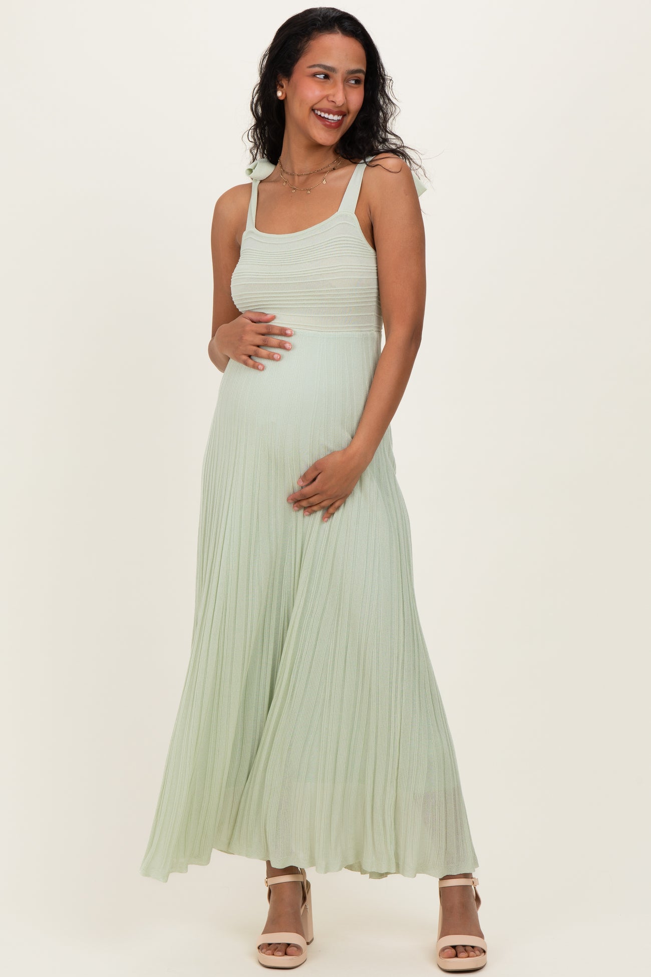 woman wearing a light green maternity dress with pleated detail and a visible baby bump