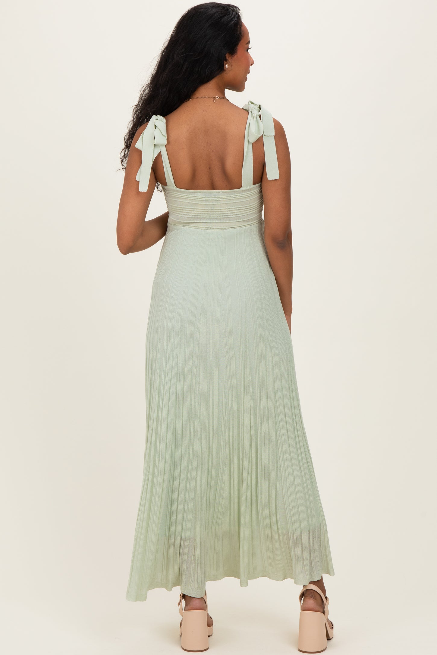 woman wearing a light green maternity maxi dress with tie straps and a fitted bodice, showing the back view