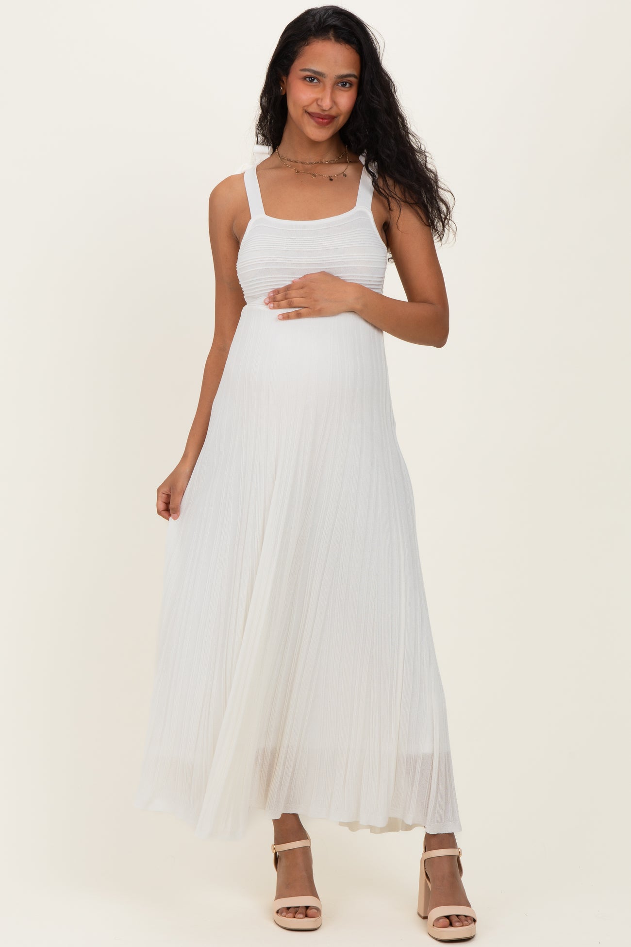 woman wearing a white pleated maternity dress and gently holding her baby bump