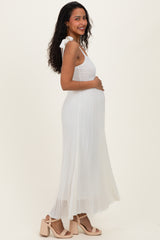 woman wearing a white pleated maternity dress with tie shoulder straps and holding her baby bump