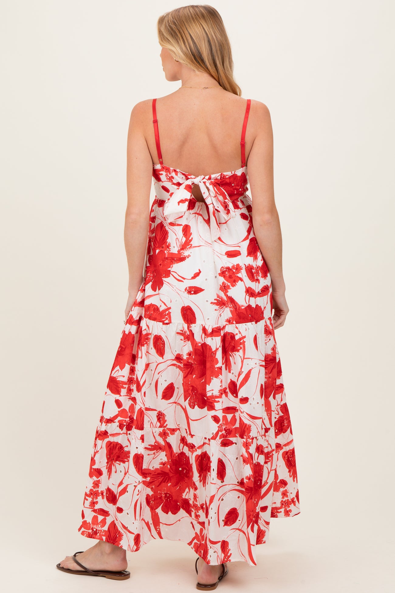 woman wearing a red and white floral print maternity maxi dress with adjustable straps and a bow detail at the back