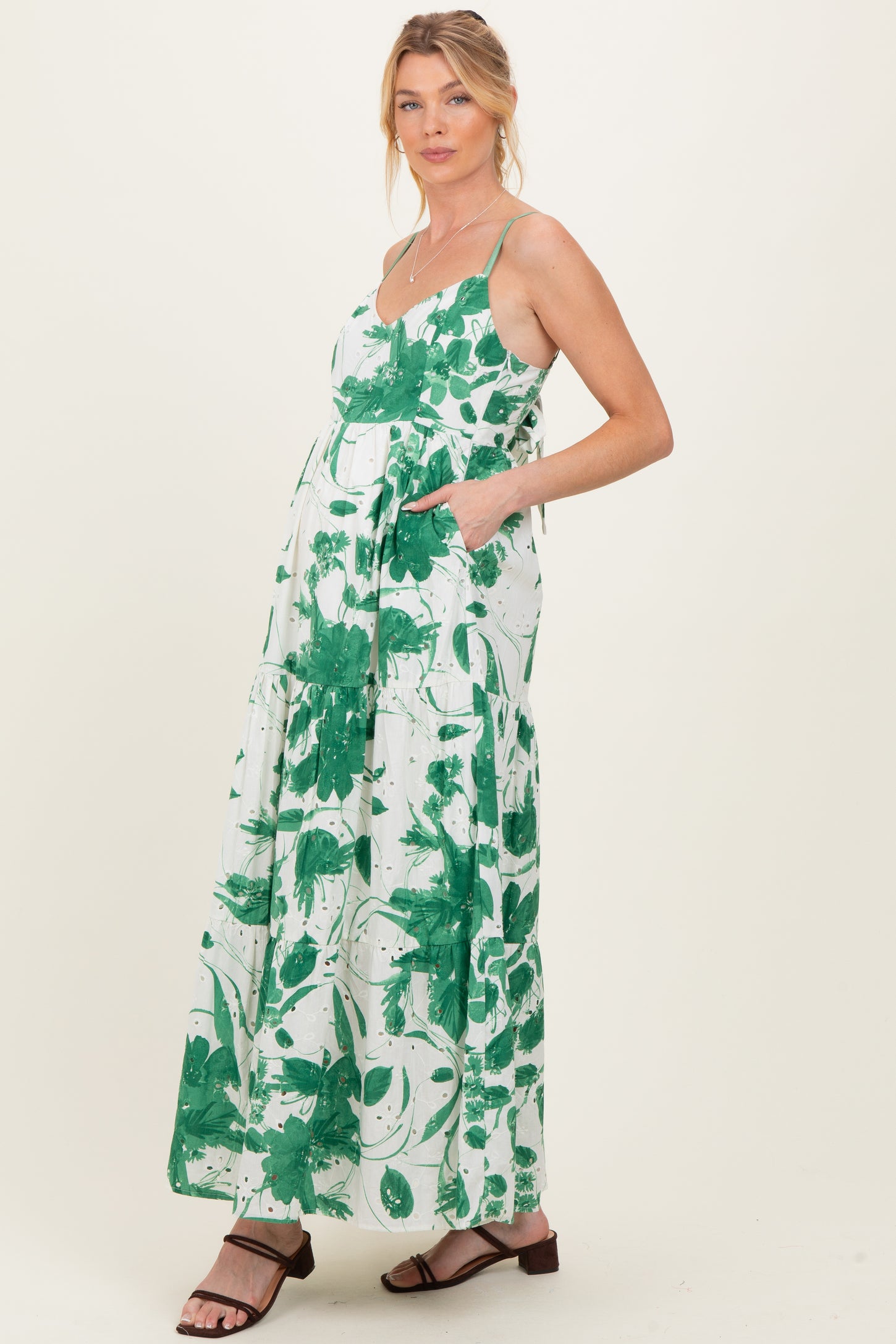 woman wearing a green and white floral maternity maxi dress with adjustable straps and pockets, displaying a baby bump