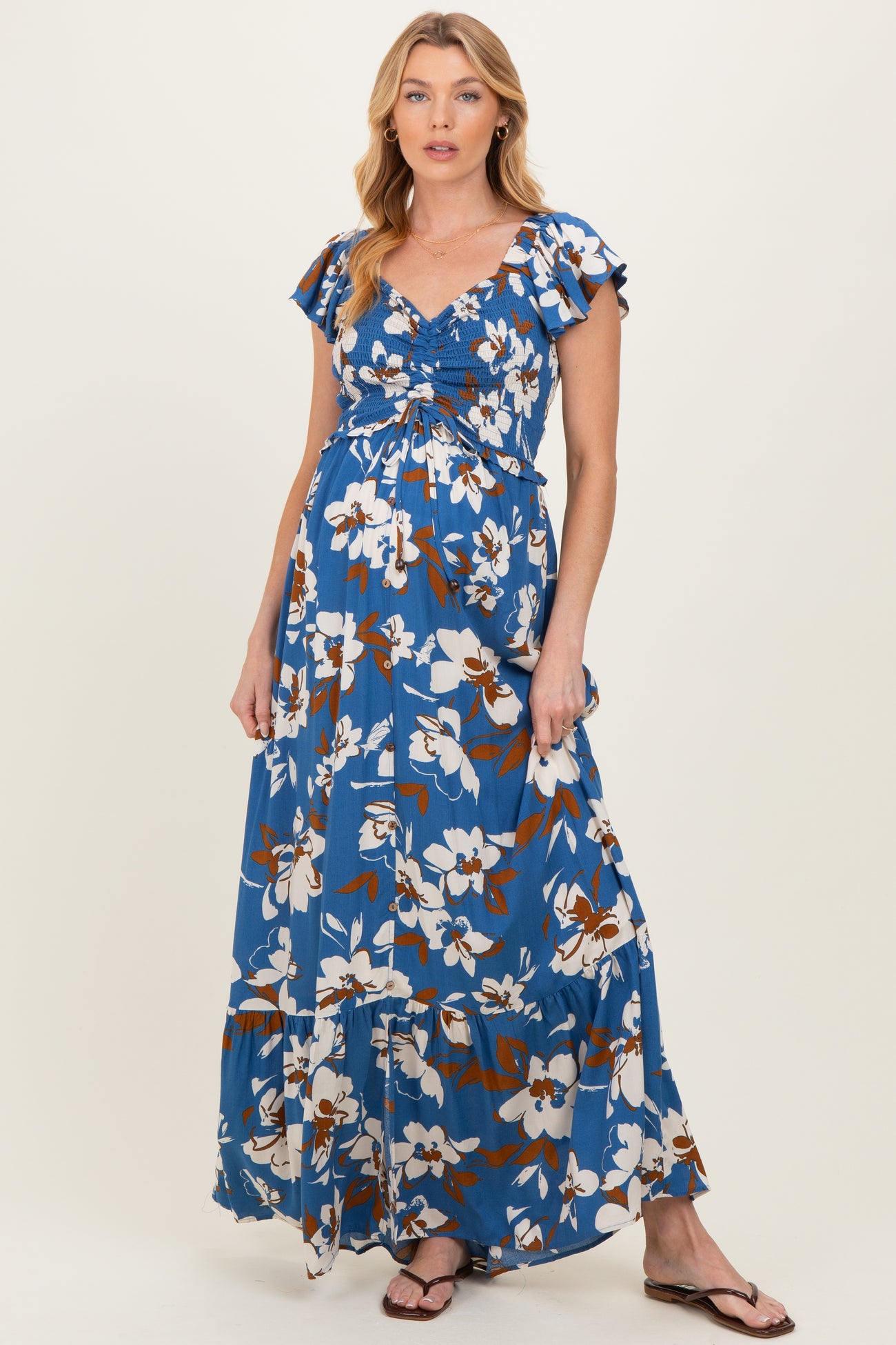 woman wearing a blue floral maternity maxi dress with short flutter sleeves and a gathered bodice, showcasing her baby bump