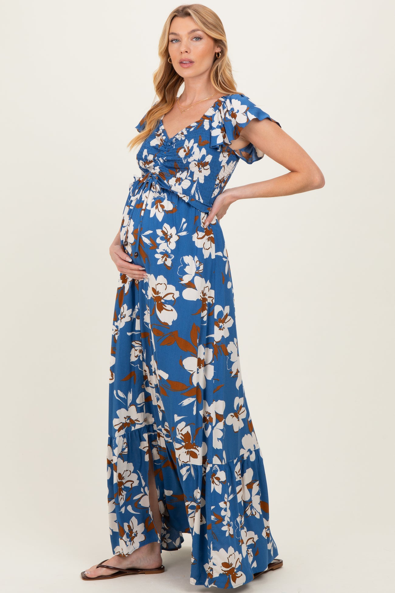 woman wearing a blue floral maternity maxi dress with short flutter sleeves and holding her baby bump