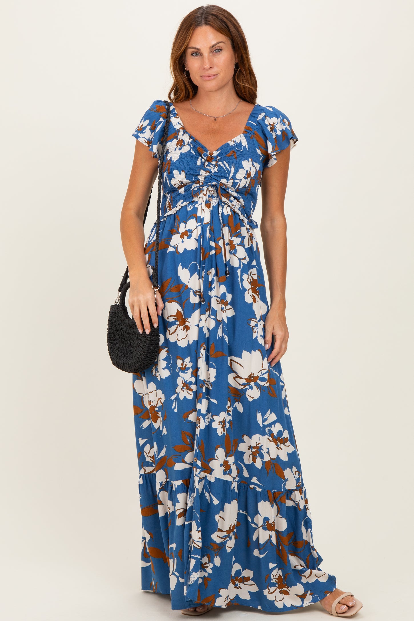 woman wearing a blue floral maxi dress with short sleeves and a gathered bodice, holding a black handbag