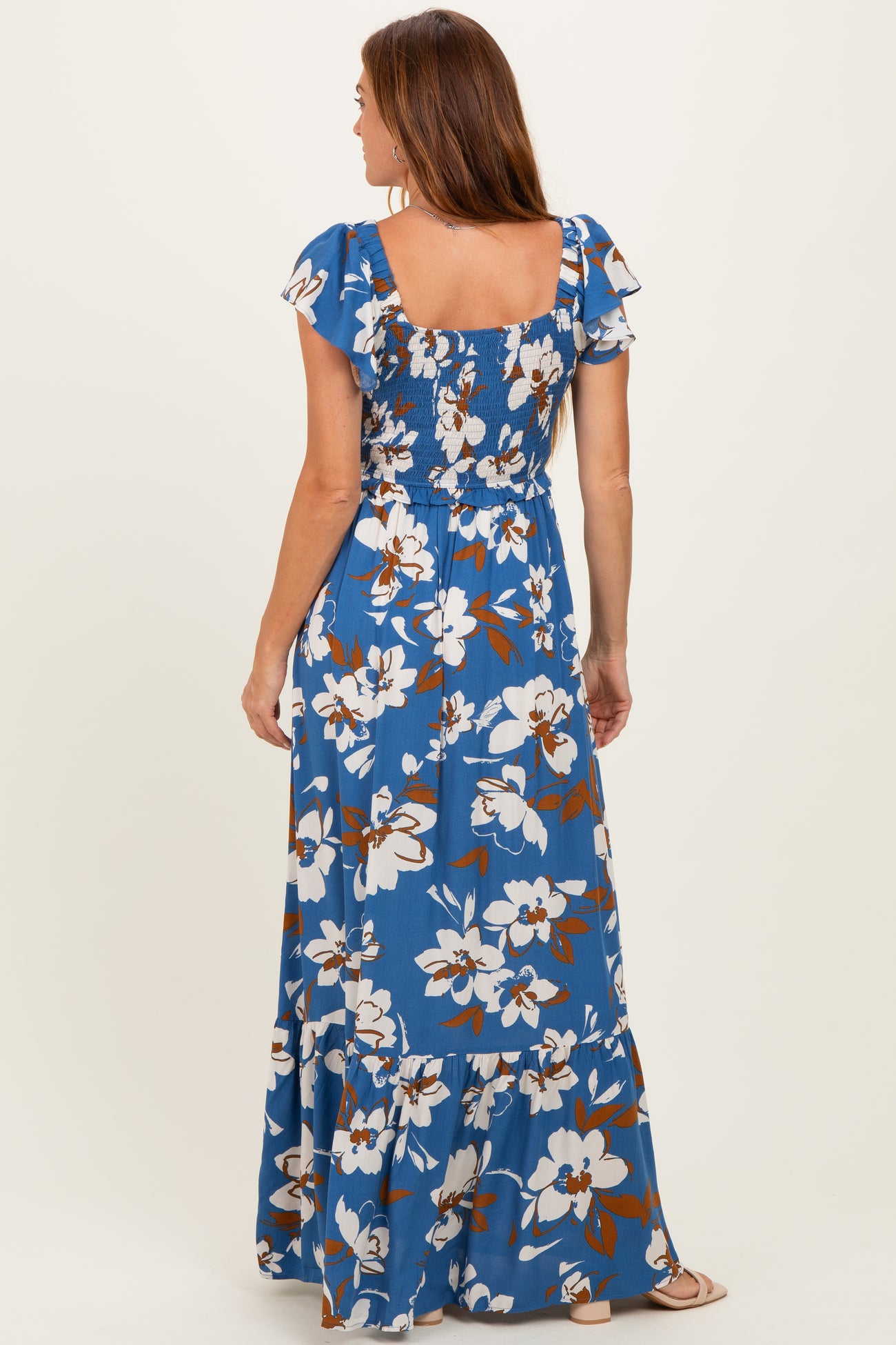 woman wearing a blue floral maxi dress with short flutter sleeves and a smocked bodice, seen from the back