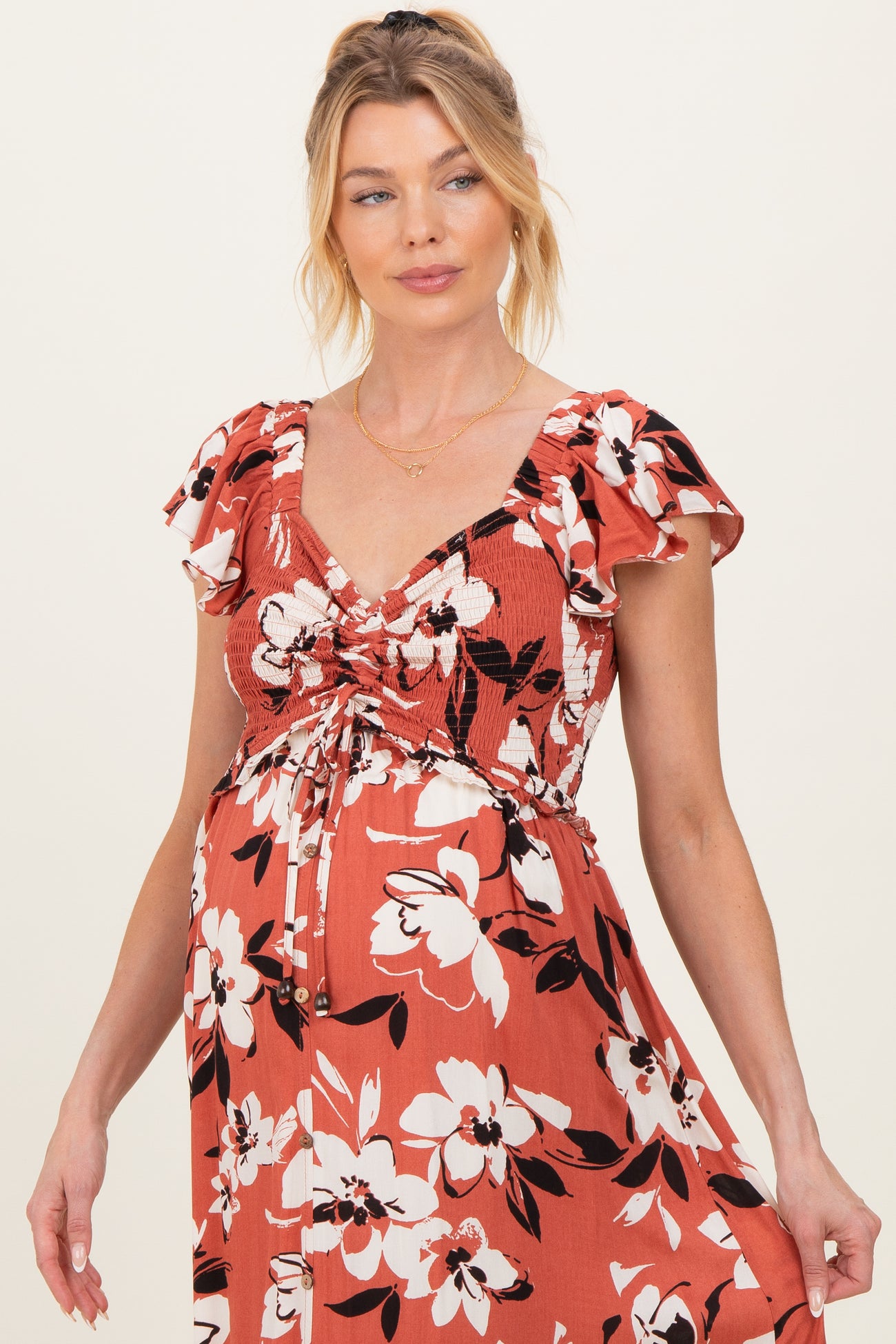 woman wearing a rust floral maternity dress with ruffled sleeves and a drawstring bodice, showing her baby bump