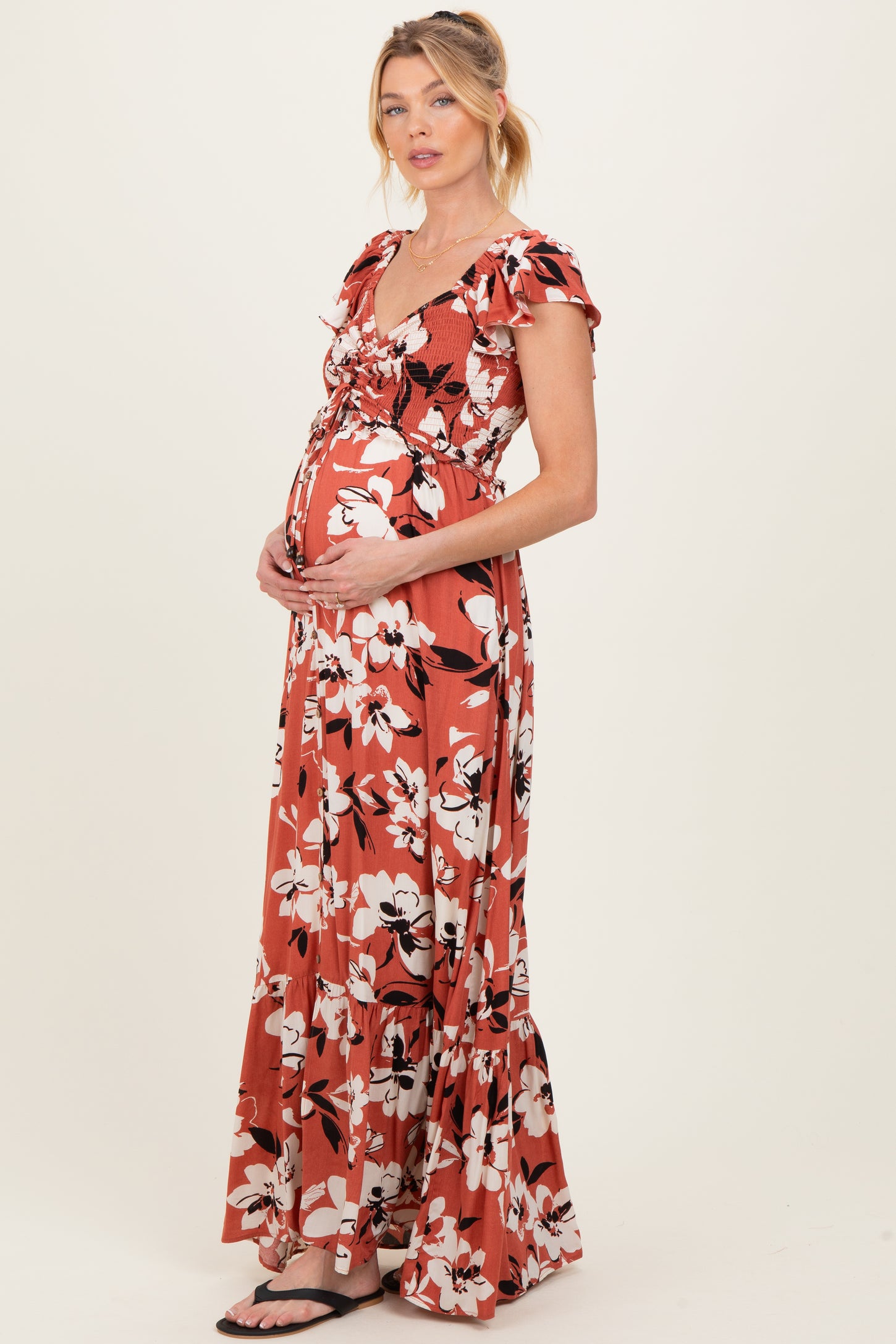 woman wearing a rust colored floral maternity maxi dress and cradling her baby bump