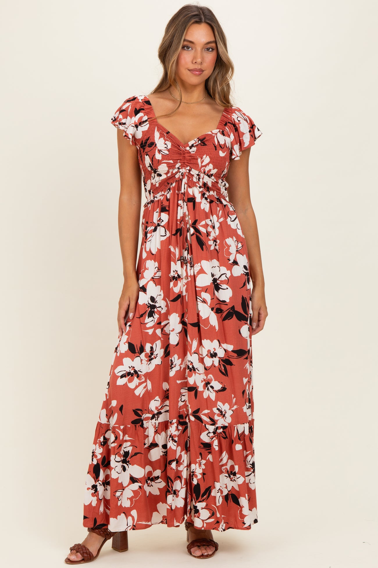 woman wearing a rust floral maxi dress with ruffled sleeves and a tiered skirt