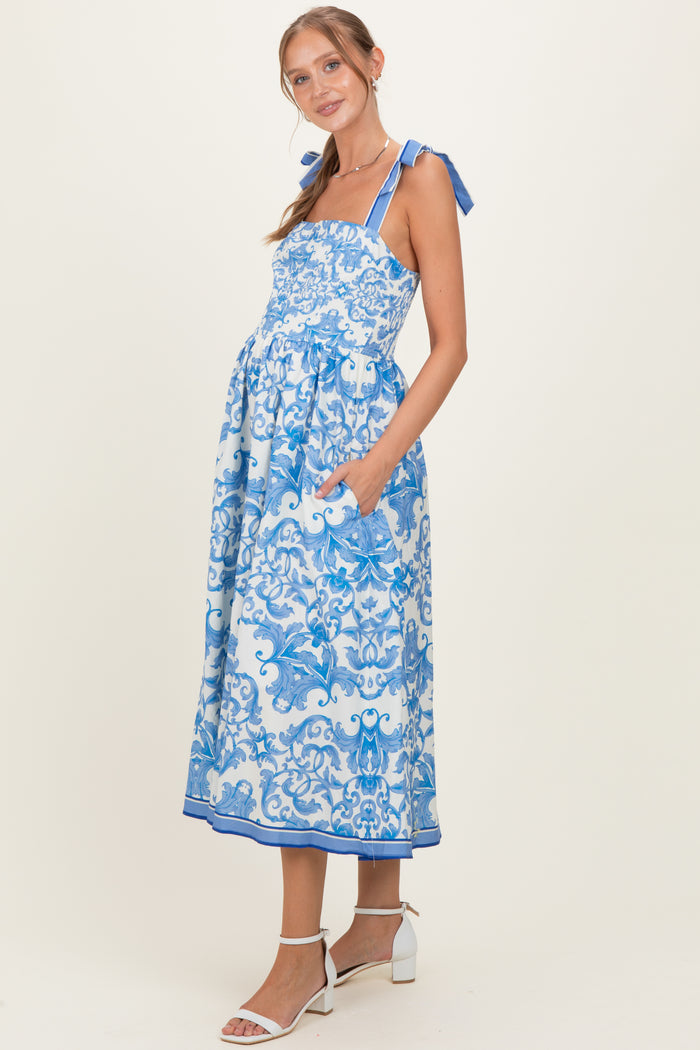 woman wearing a blue and white floral print maternity dress with tie straps and pockets, showcasing her baby bump