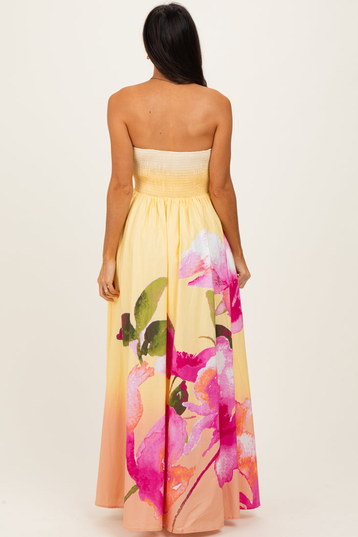 woman wearing a strapless yellow maxi dress with a floral print in pink and green at the hem