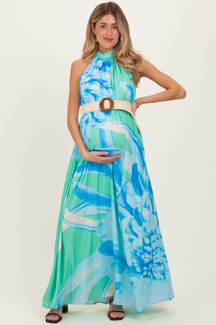 woman wearing a blue and green floral maternity maxi dress, holding her baby bump and styled with a belted waist