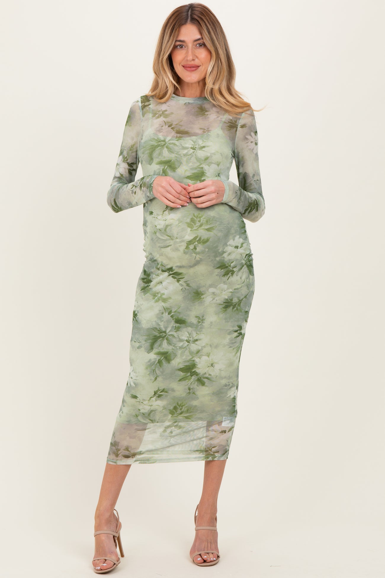 woman wearing a sheer green floral maternity dress with long sleeves and a fitted silhouette, showcasing a baby bump