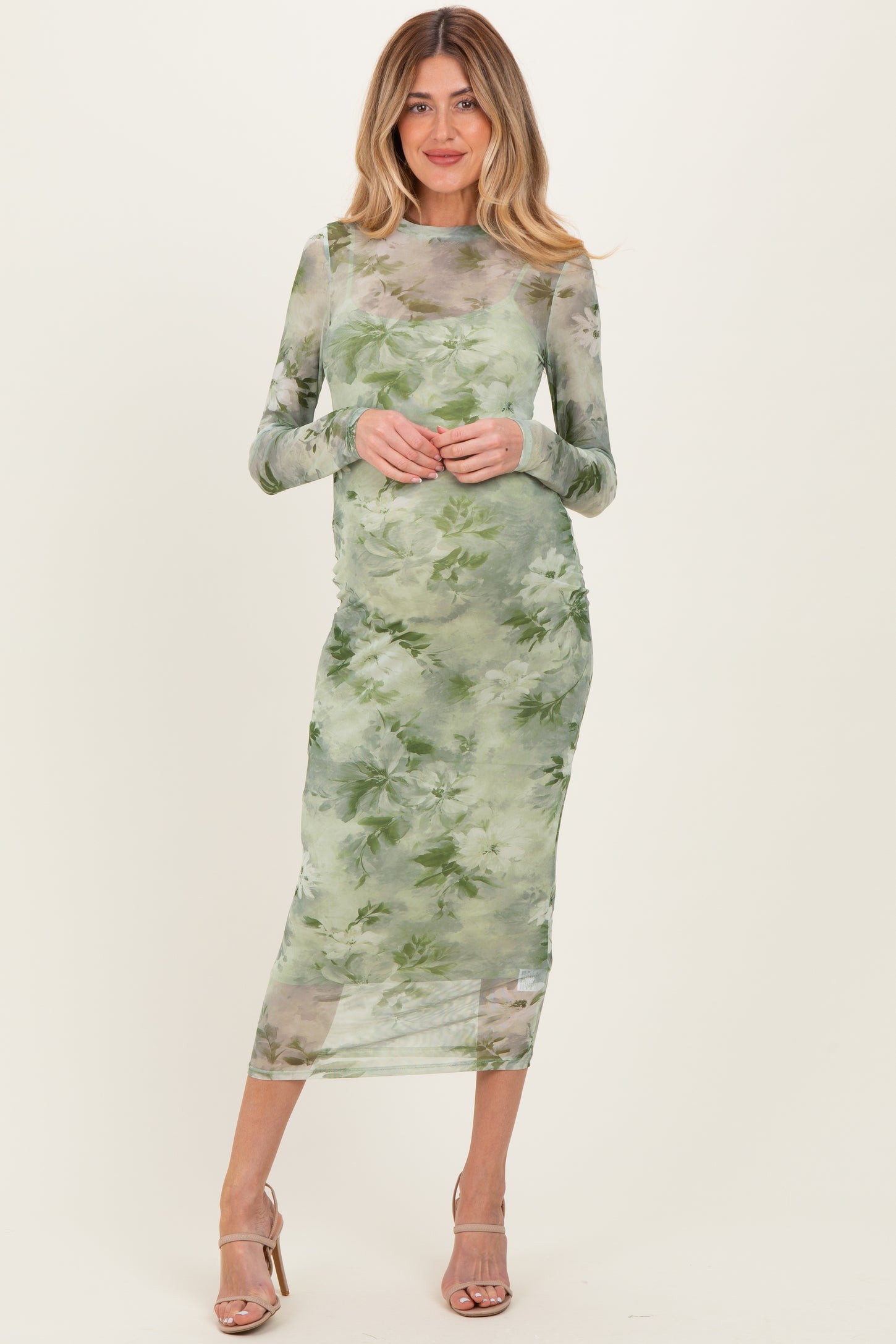 woman wearing a sheer green floral maternity dress with long sleeves and a fitted silhouette, showcasing a baby bump