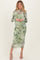 woman wearing a sheer green floral maternity dress with long sleeves and a fitted silhouette, showcasing a baby bump