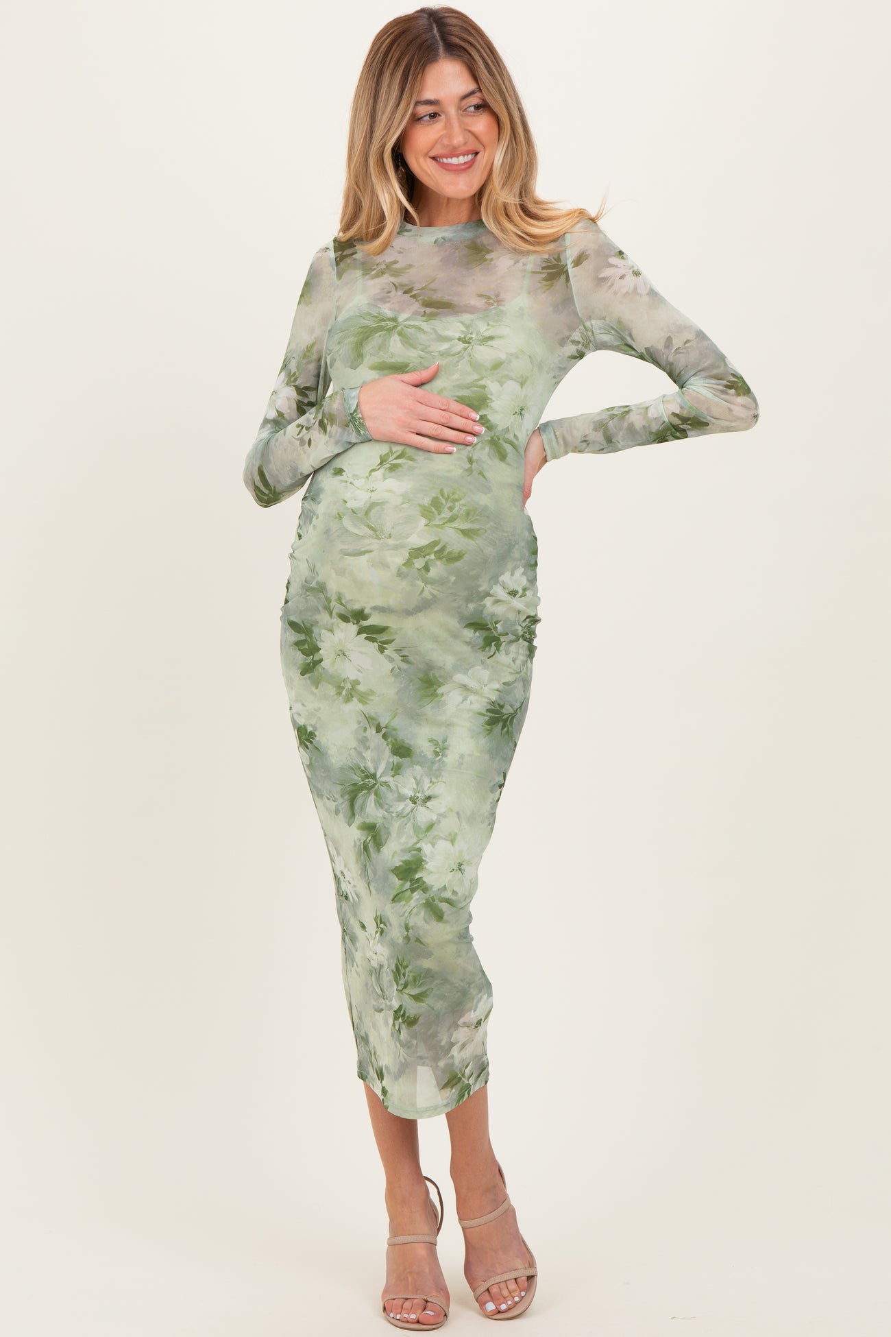 woman wearing a sheer green floral maternity dress and holding her baby bump