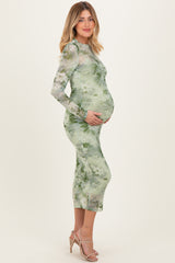 woman wearing a green floral print maternity dress with long sleeves and a visible baby bump