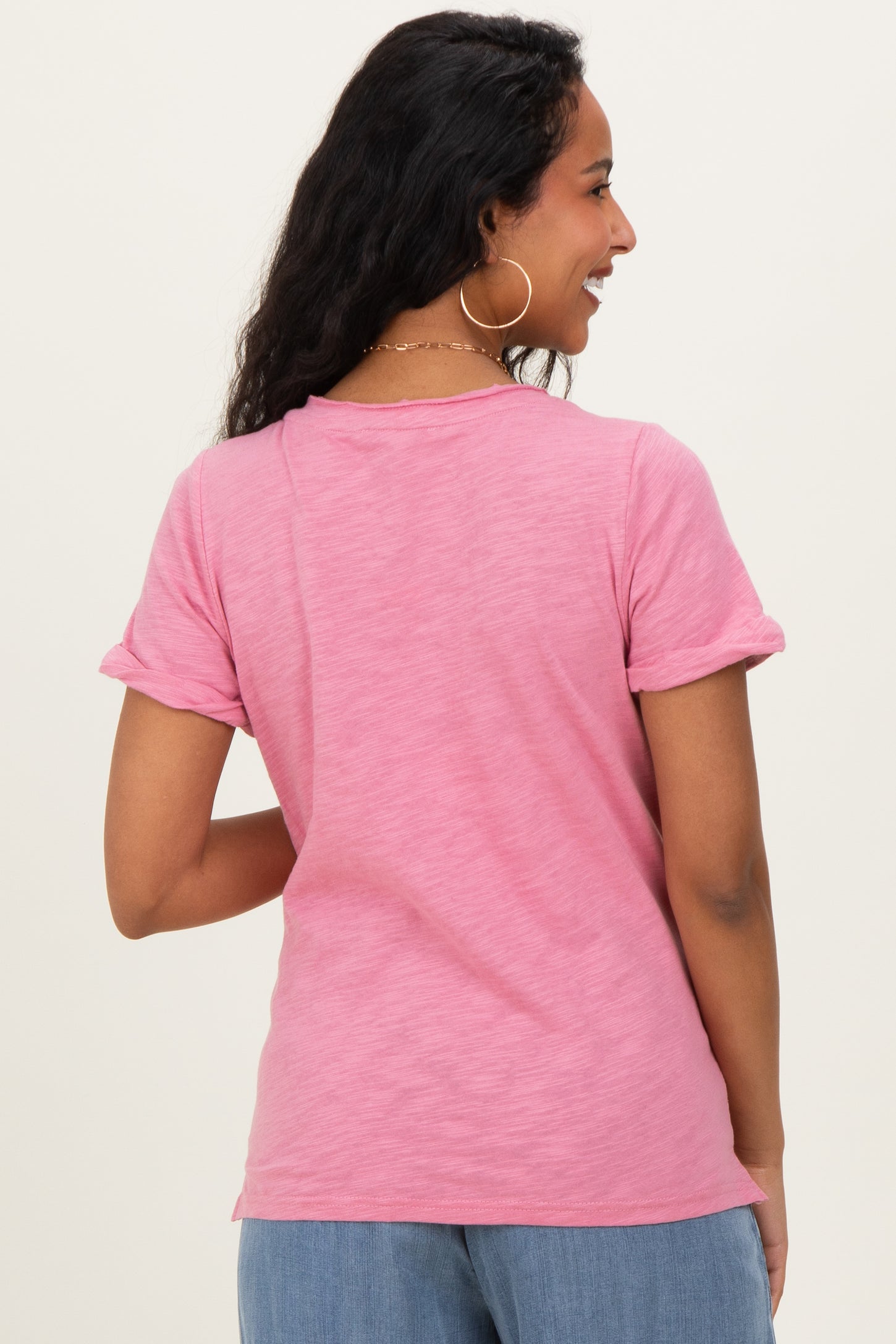 woman wearing a pink short sleeve maternity tee, viewed from the back, with rolled cuffs and a relaxed fit