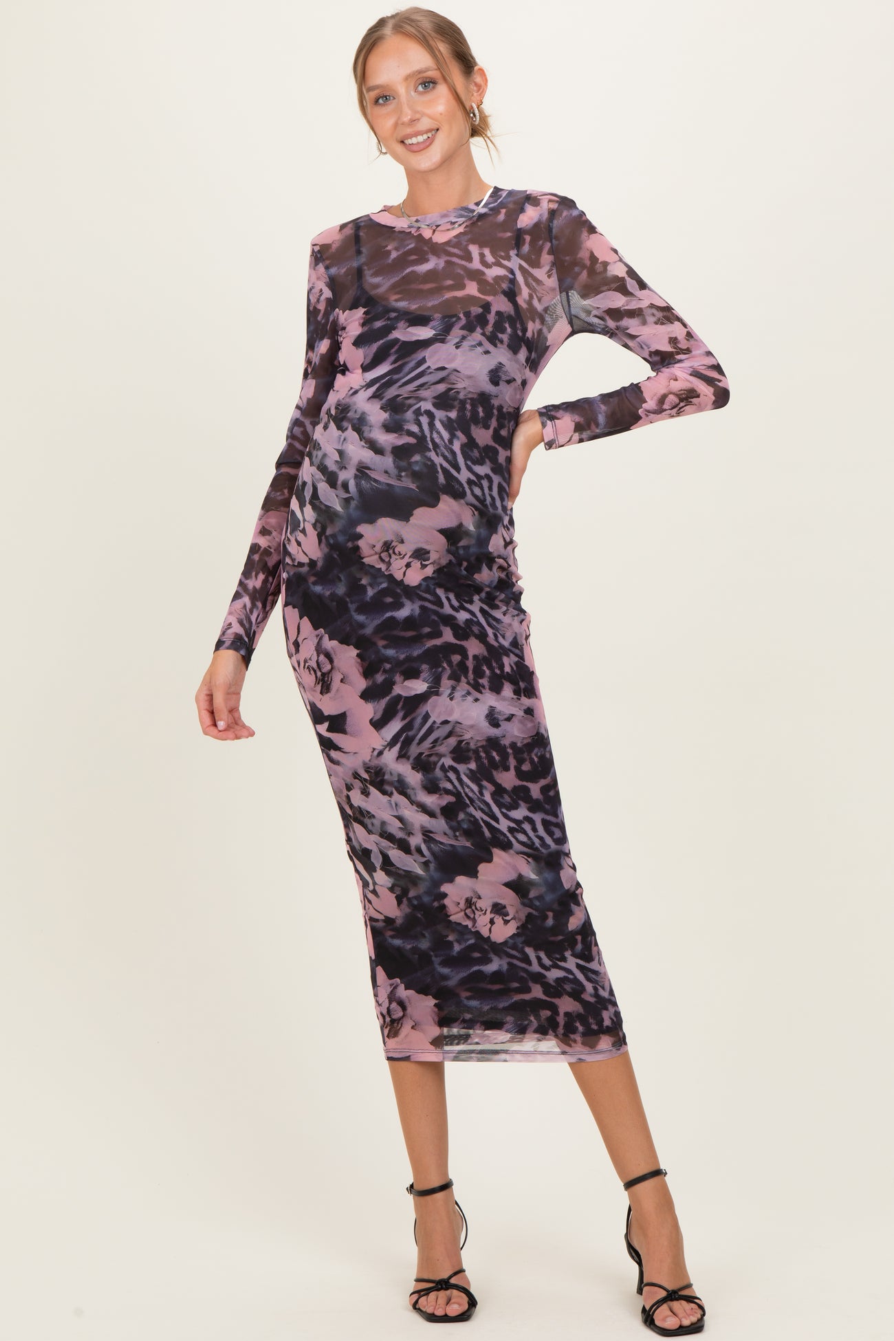 woman wearing a sheer long sleeve maternity dress in purple and black floral print, showing baby bump