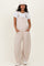 woman wearing a striped beige maternity overall with wide legs and a white t-shirt, smiling and posing with hands in pockets